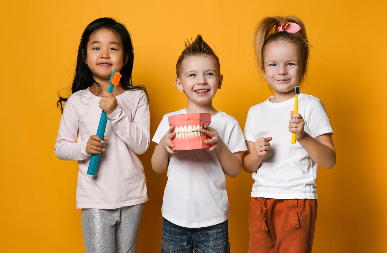 Three children holding toothbrushes and a large model of teeth
