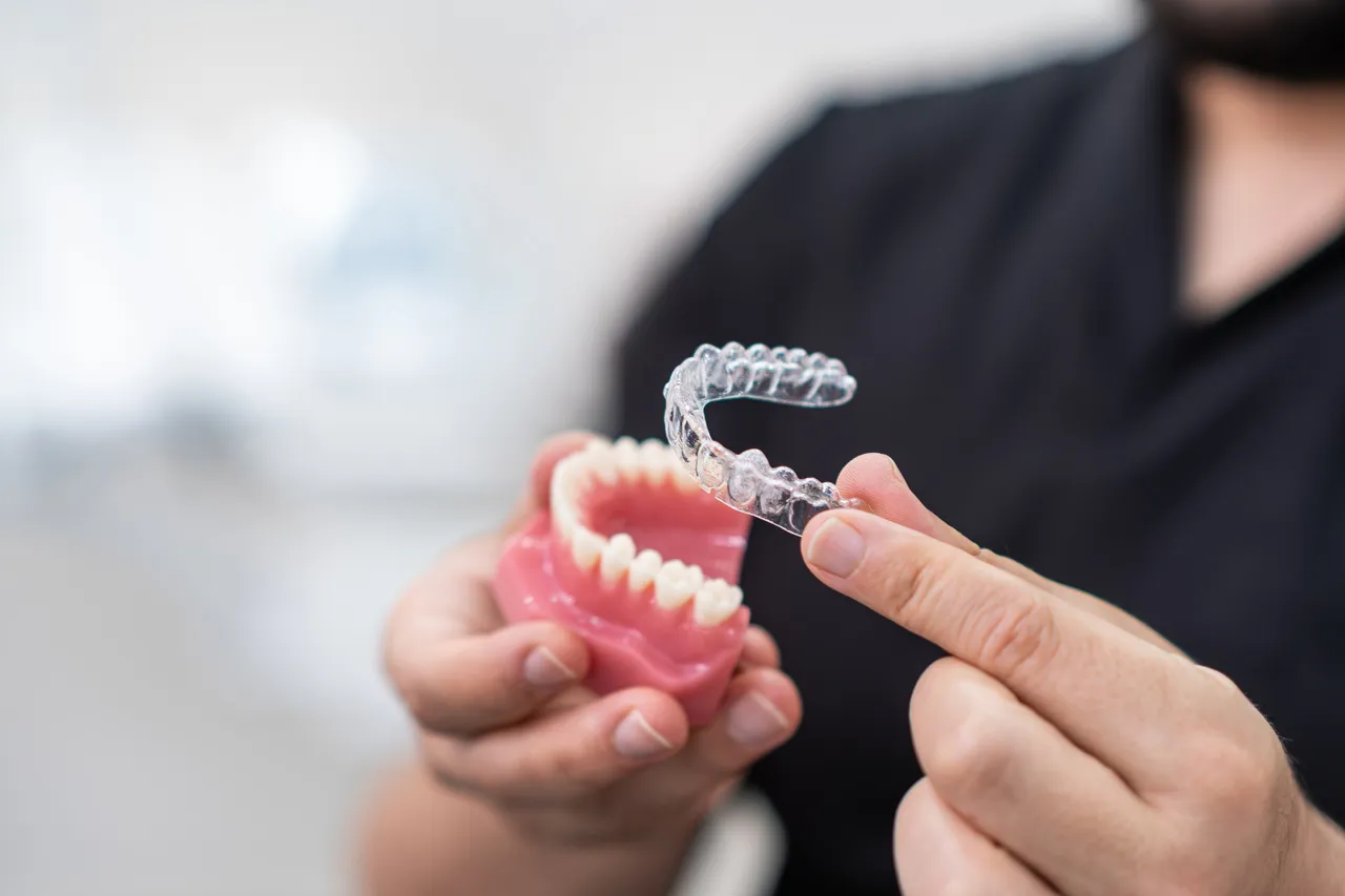 A clear aligner tray held beside a dental model
