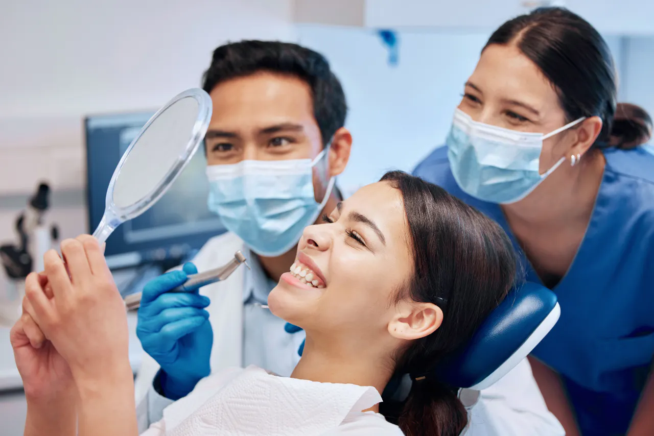 A patient checking her clean teeth in a hand mirror after a cleaning