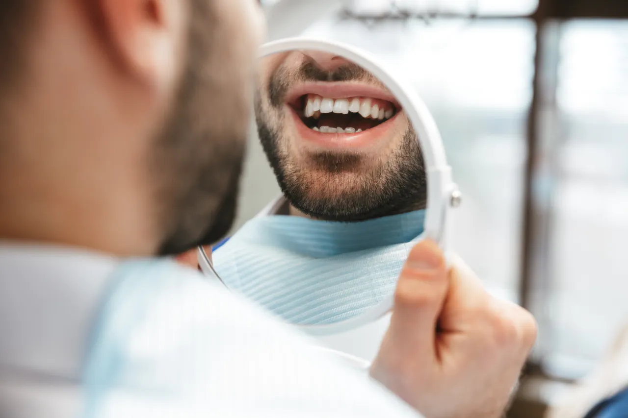 A man checking his repaired tooth in a hand mirror