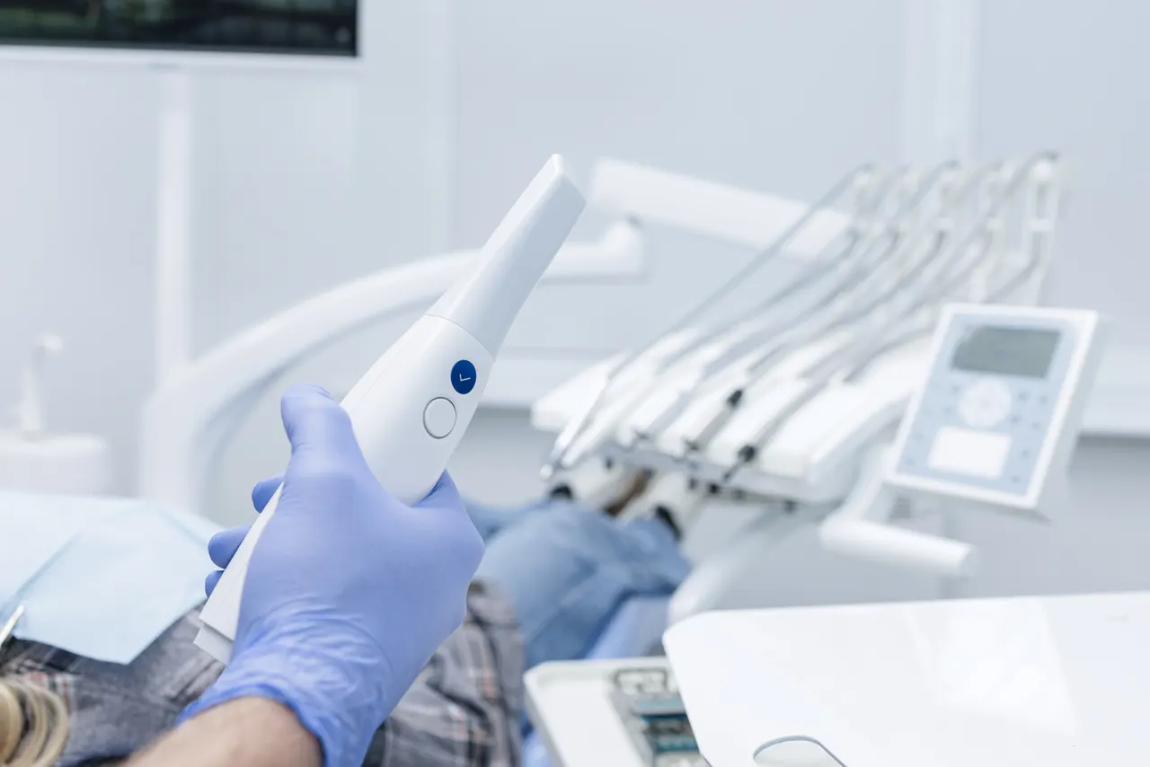 A gloved hand holding a digital impression scanner wand