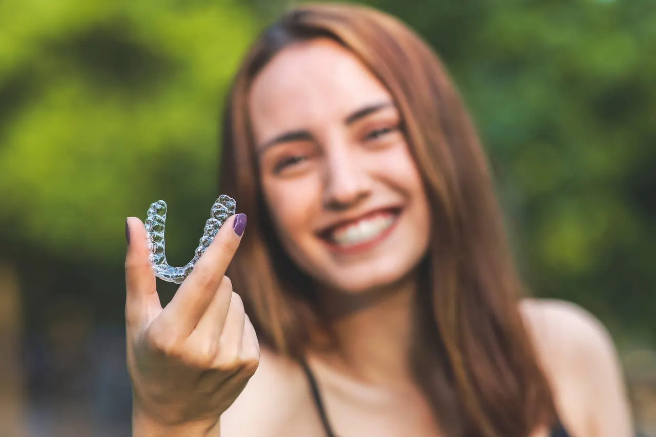 A smiling patient holding her clear aligner tray
