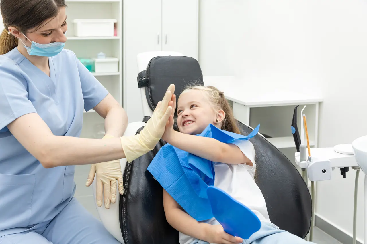 A hygienist high-fiving a young patient in the dental chair