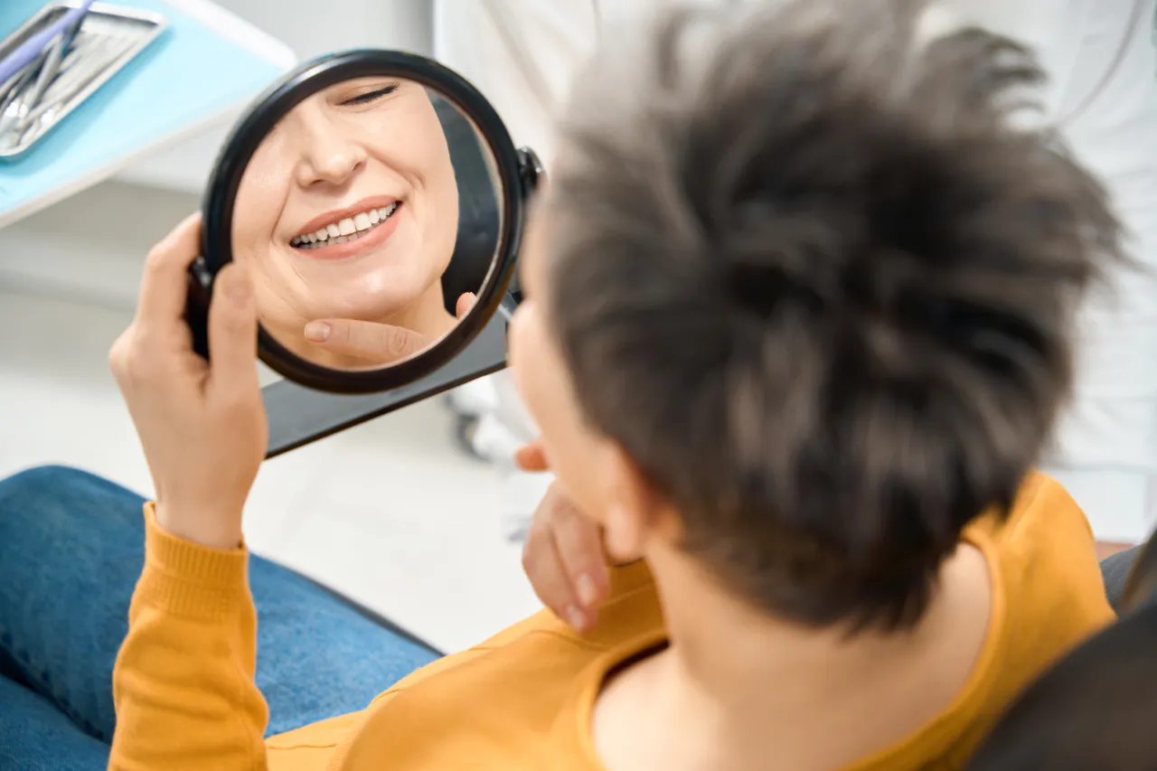 A patient admiring her new smile in a hand mirror